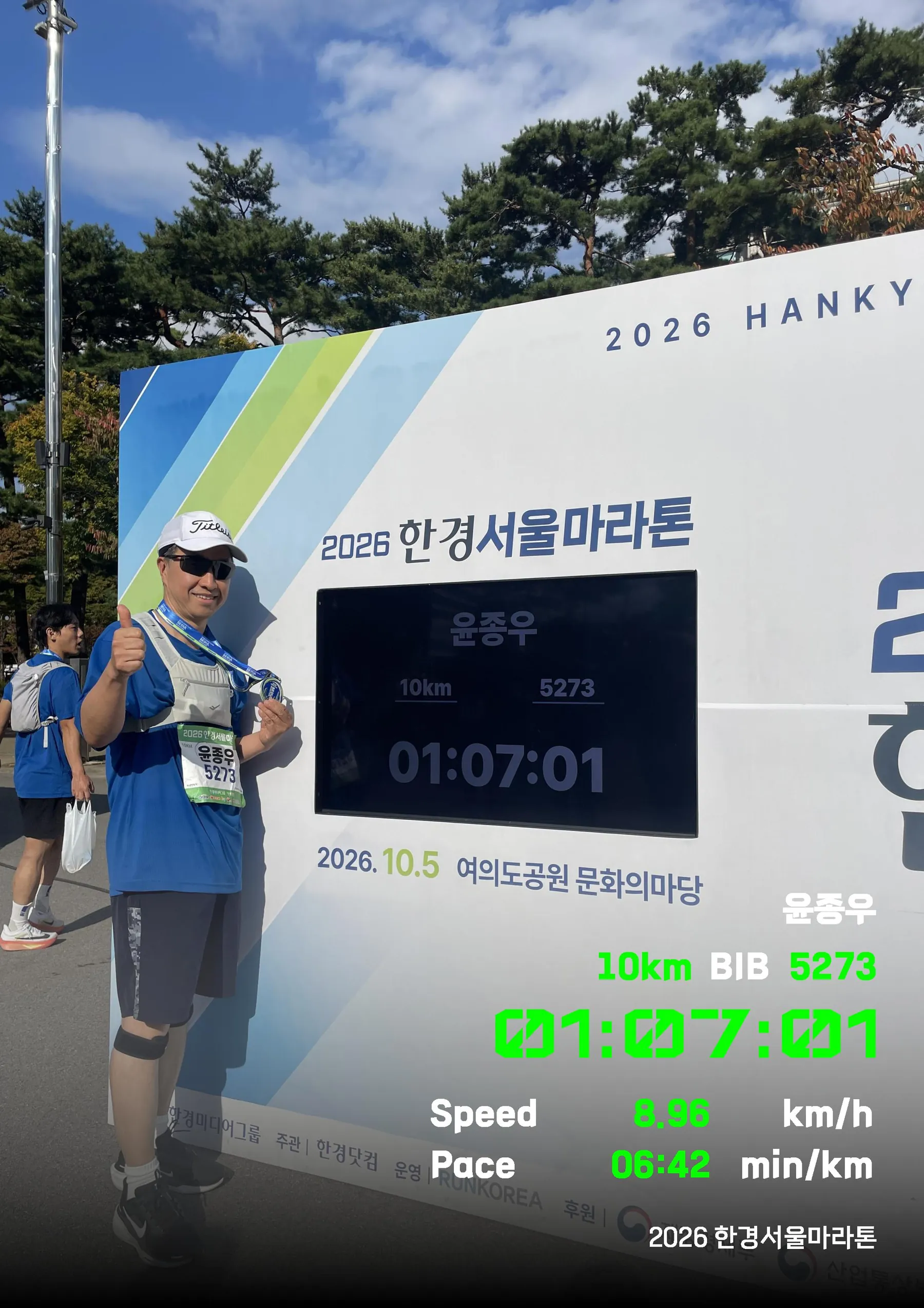 2026 한경서울마라톤 10km 완주 기록판 앞에서 엄지를 들어 보이는 윤종우 — 01:07:01