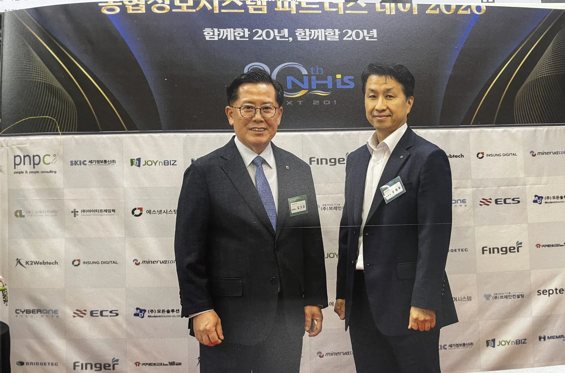 ‘함께한 20년, 함께할 20년’ 포토월 앞에서 농협정보시스템 관계자와 나란히 선 윤종우 이사